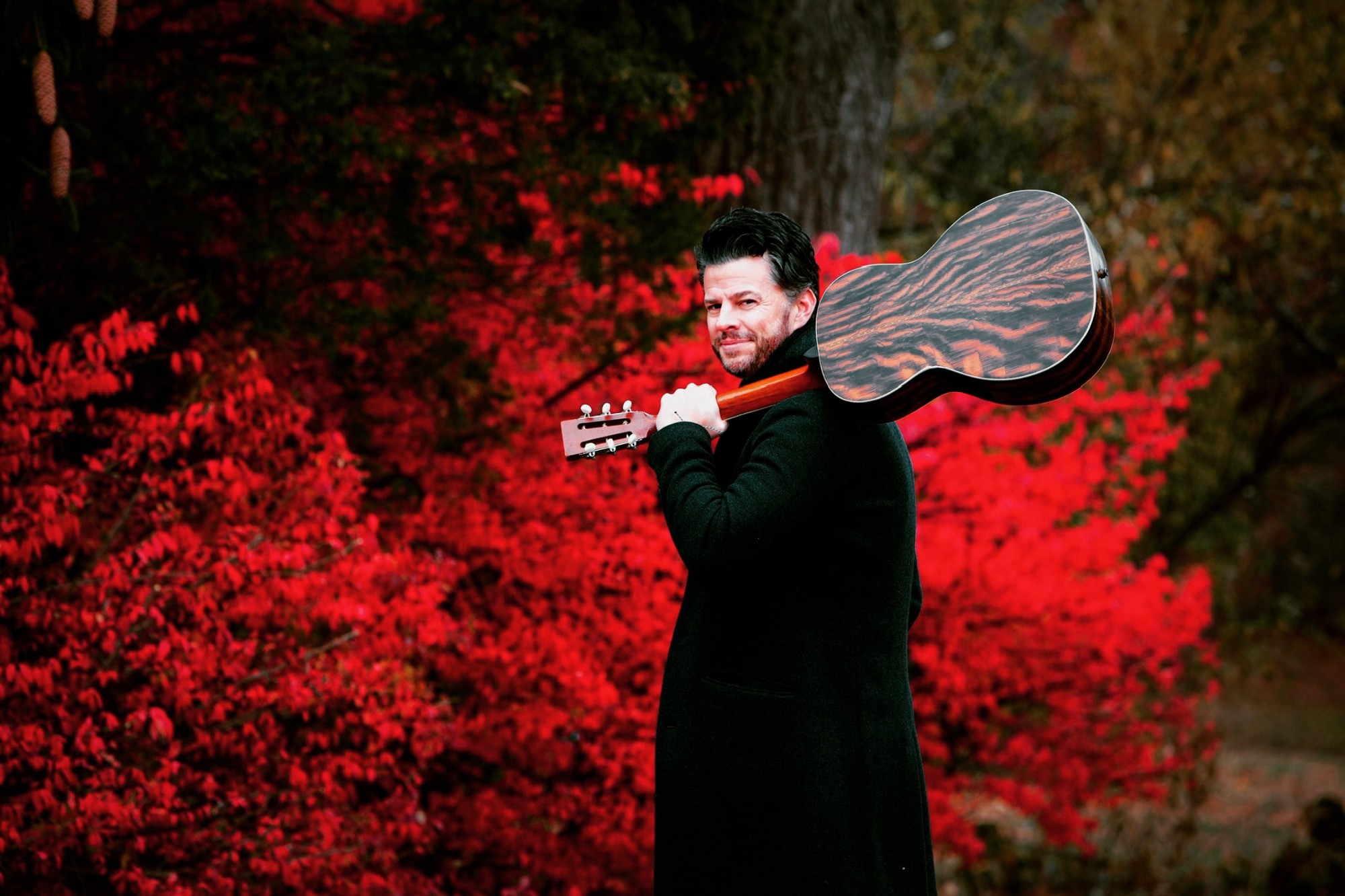 Matt Dorsey with his guitar among red autumn leaves