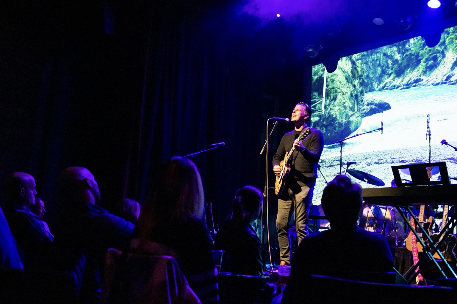 Matt Dorsey singing and playing guitar on stage under blue lights